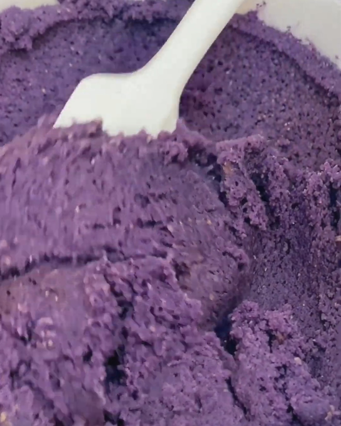 Syvän purppuranvärinen ube-cookietaikina käännellään valkoisella lastalla UBE NOLIA® ubejauhein lisäämisen jälkeen