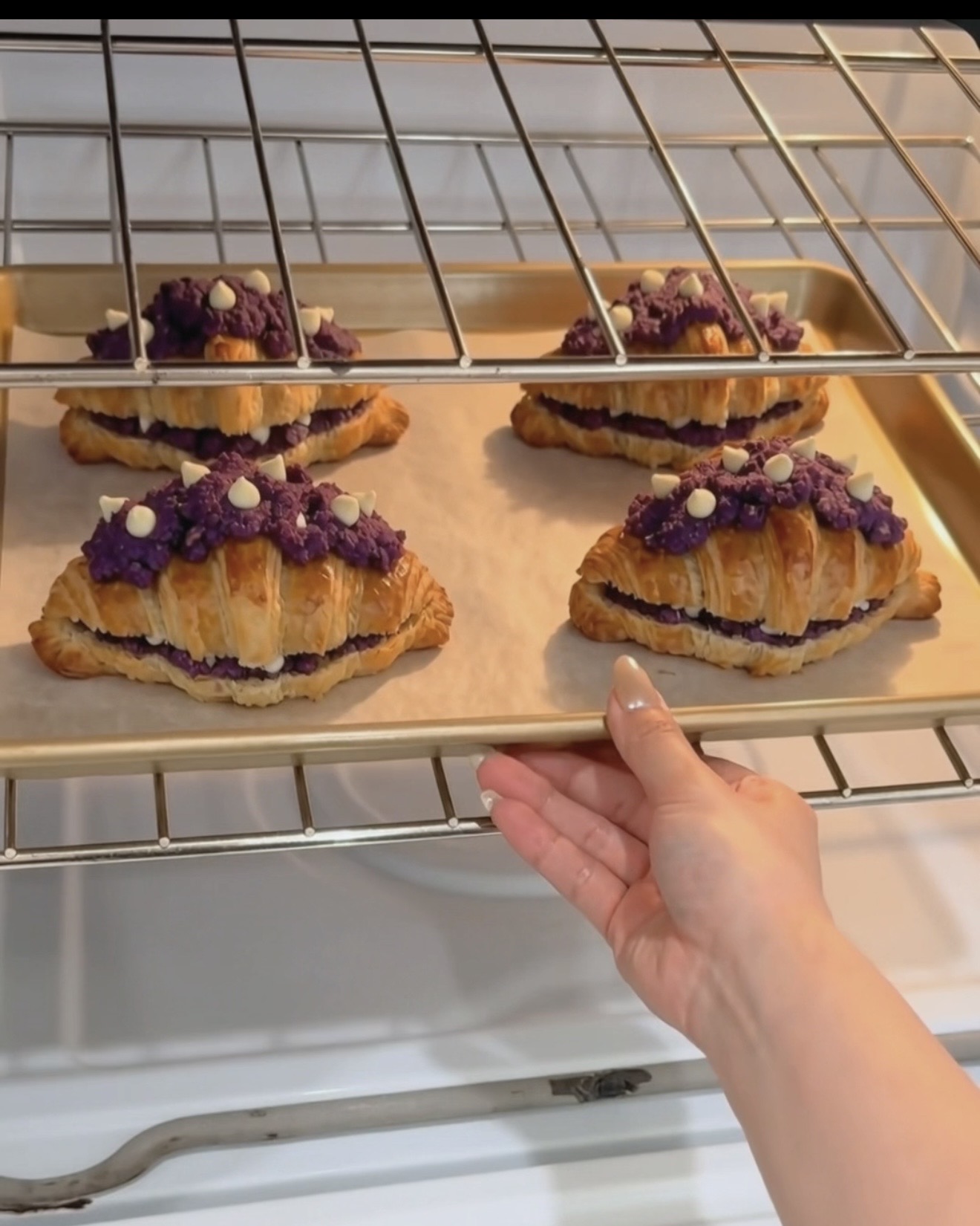 Pellillinen UBE NOLIA® ube crookiejä juuri uunista otettuna, kullanruskeat croissant-kerrokset ja purppura ube (purple yam) cookie-täyte valkosuklaahipuilla