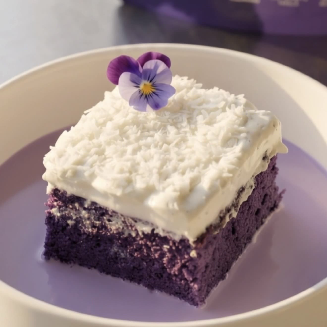 Slice of ube coconut tres leches cake topped with coconut whipped cream and shredded coconut, ready to serve | Ube Nolia