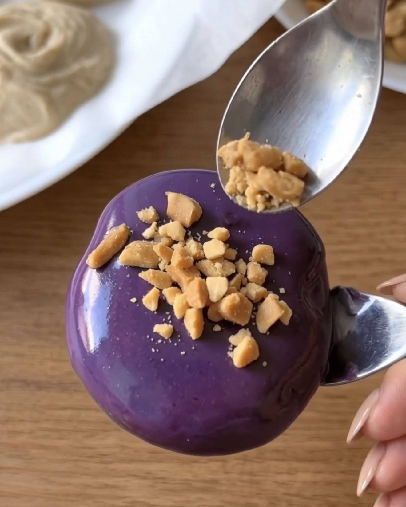 Murskattuja paahdettuja maapähkinöitä ripoteltuna purppuraan ube-valkosuklaalla päällystettyyn Ube Nolia -pakastejogurttipalaan