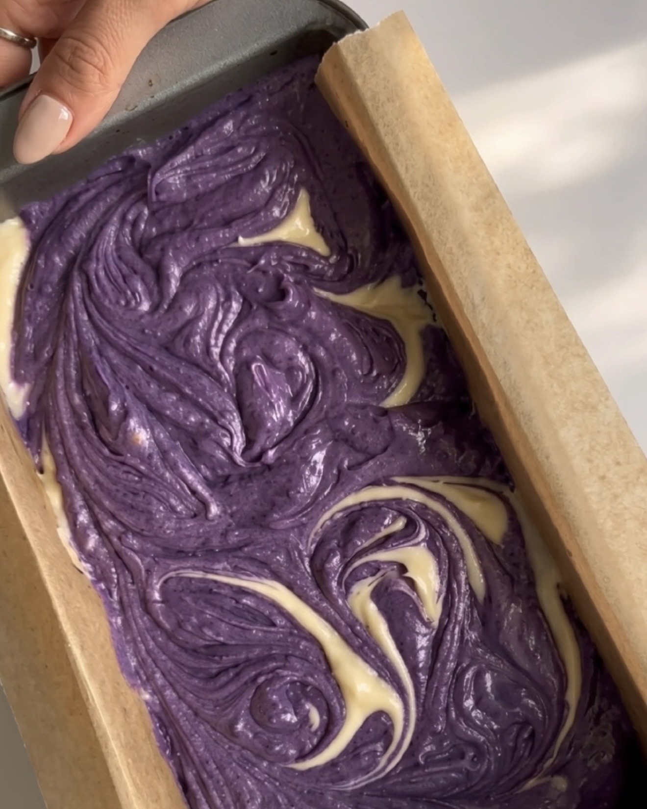 Violetit ja vaniljaiset taikinat pyöritettyinä marmorikuvioon leipävuoassa Ube Nolia ube-marmoripoundkakkuun