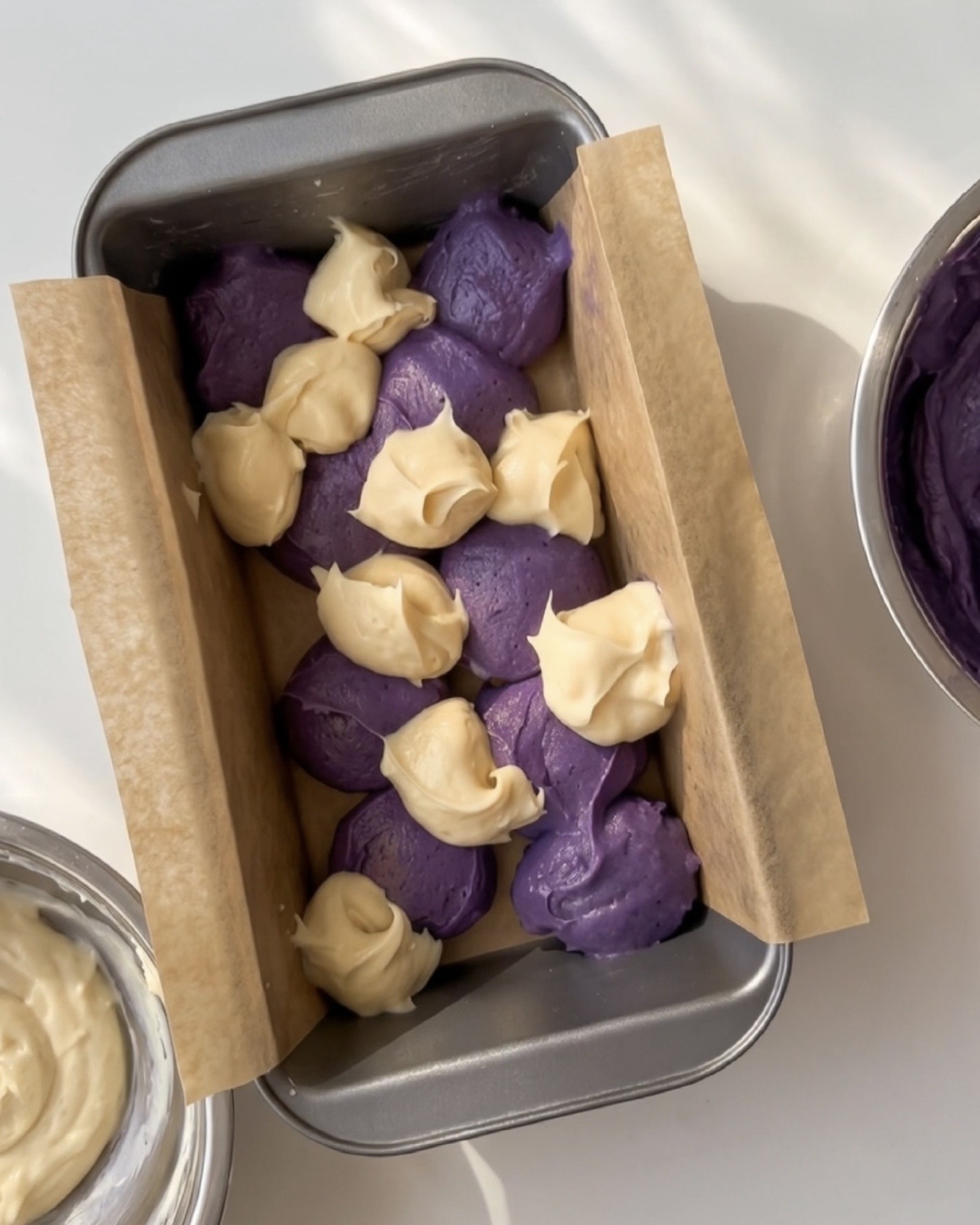 Kauhallisia violettia ube-taikinaa ja vaniljataikinaa vuorotellen vuoratussa leipävuoassa Ube Nolia ube-marmoripoundkakkuun