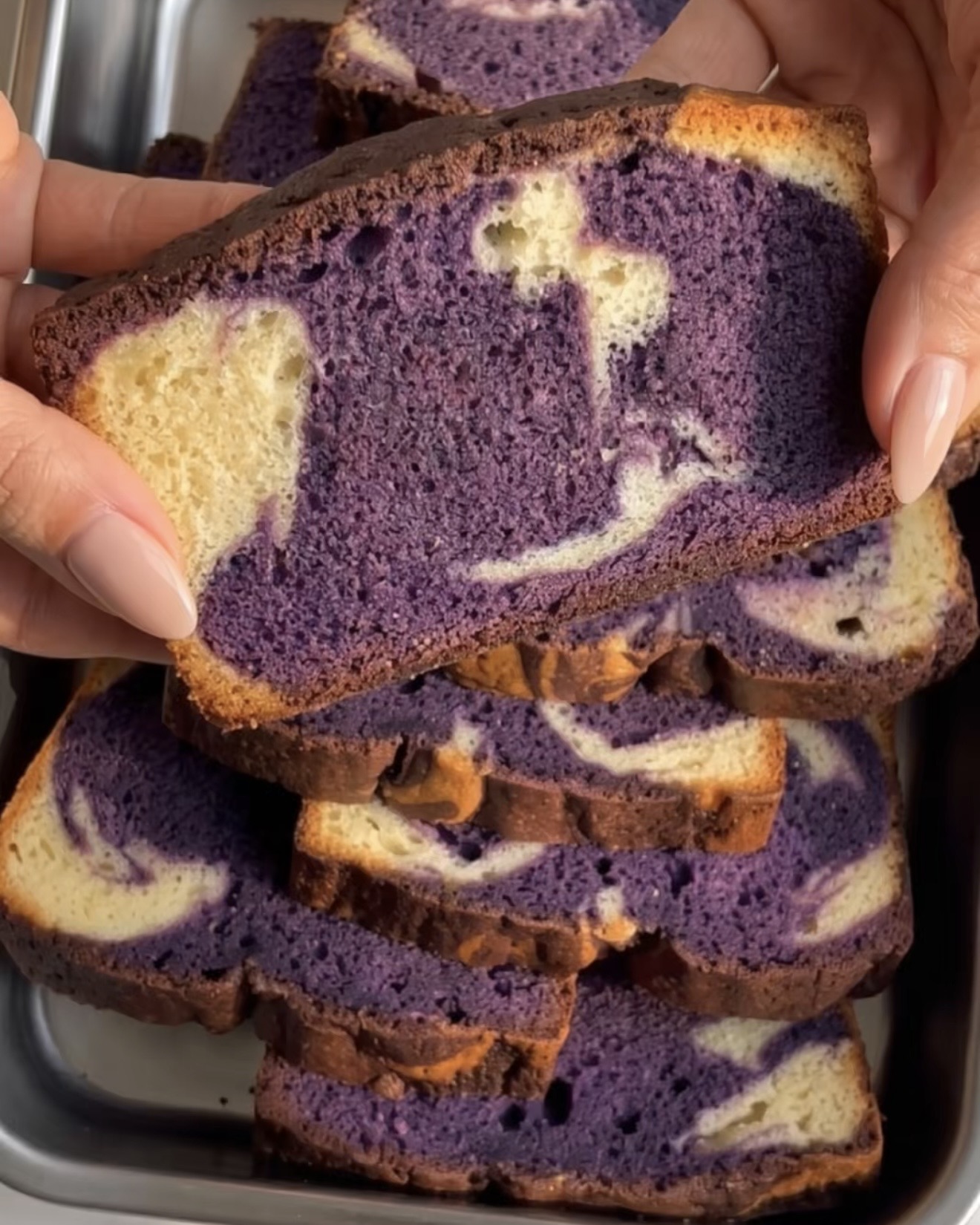 Käsi pitää viipaletta ube-marmoritiikerikakusta, jossa on violetti ja vaniljapyörre, paistettu UBE NOLIA® ubejauheilla