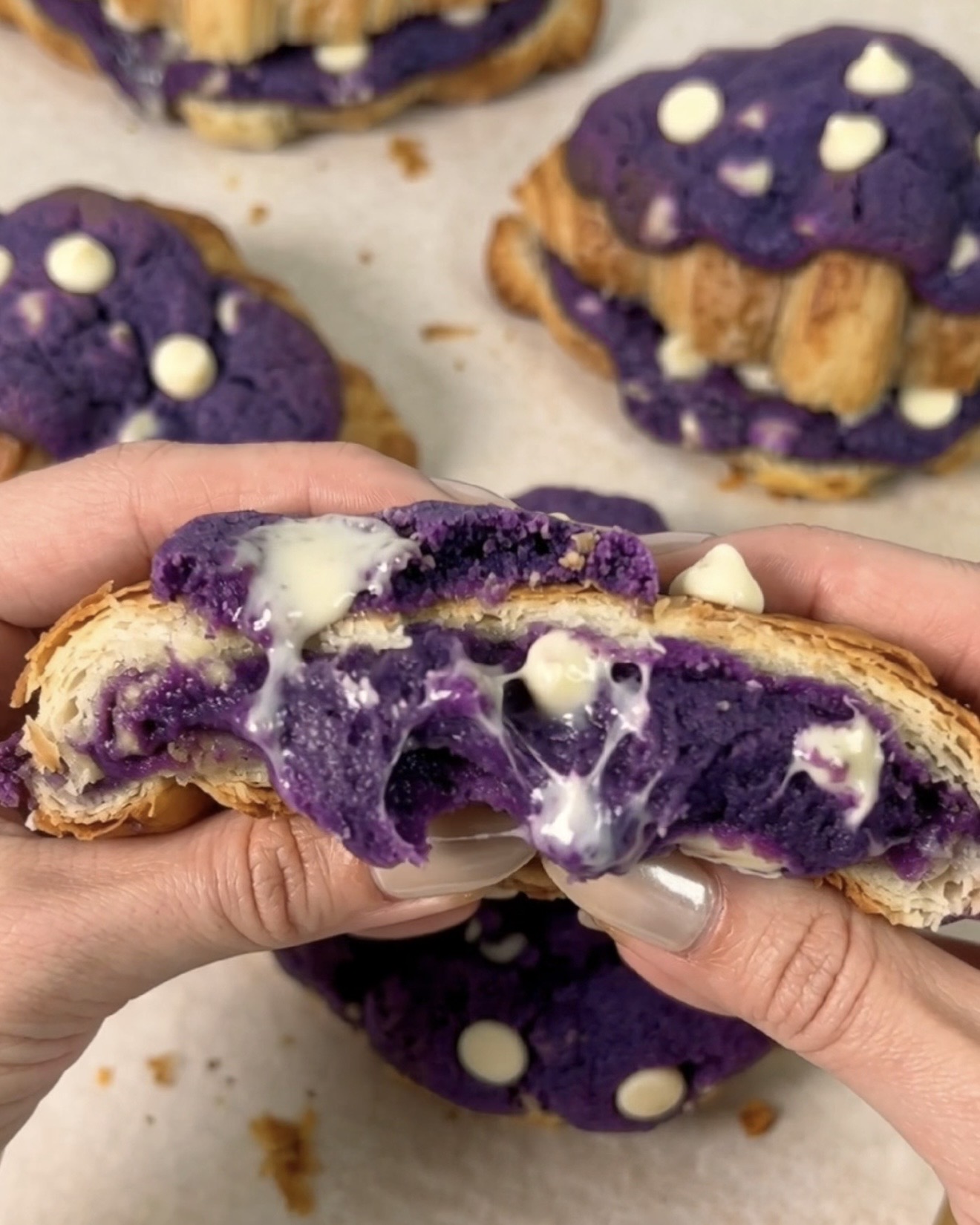 Vasta paistetut UBE NOLIA® ube crookiet avattuina paljastamaan sulan purppuranvärisen ube (purple yam) valkosuklaa cookie -keskuksen valuen kullanruskeiden croissant-kerrosten välistä