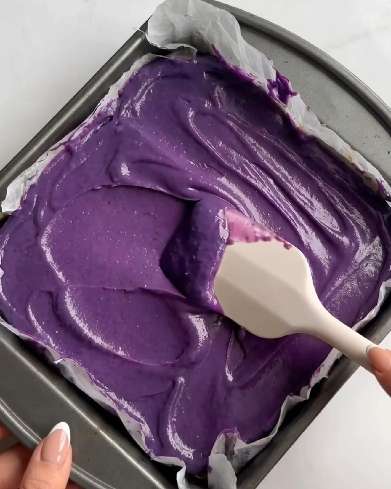 Eloisaa purppuraa ube-valkosuklaaganachea levitetään pistaasikataifikerroksen päälle Ube Dubai -suklaabrowniepaloja varten Ube Nolia -brändiltä