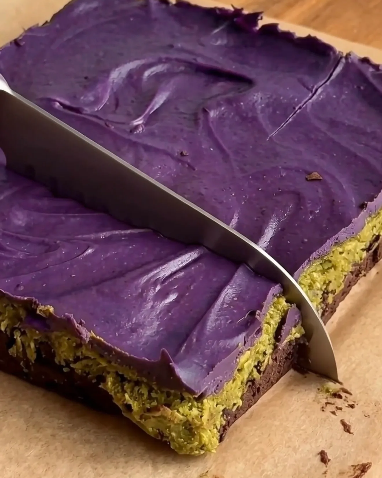 Jäähtyneiden Ube Dubai -suklaabrowniepalojen leikkaaminen näyttää brownie-, pistaasikataifi- ja ube-valkosuklaakerrokset Ube Nolia -brändiltä